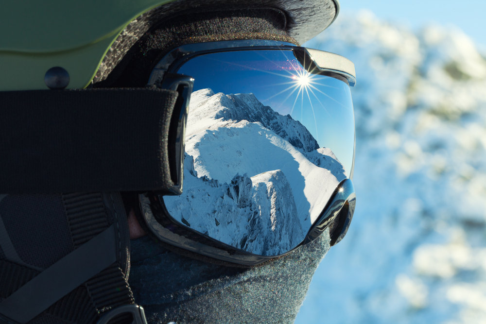Ski goggles with a reflection of snow-covered mountains in it.